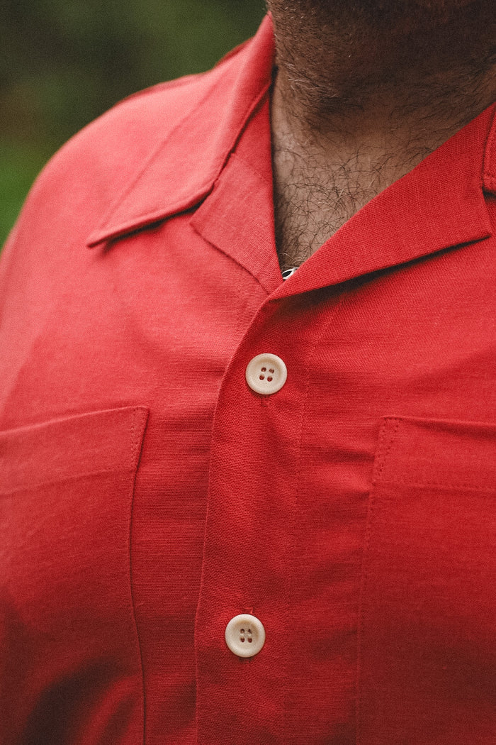 Close-up of a person wearing a red short-sleeve camp-collar button-up shirt with cream-colored buttons.