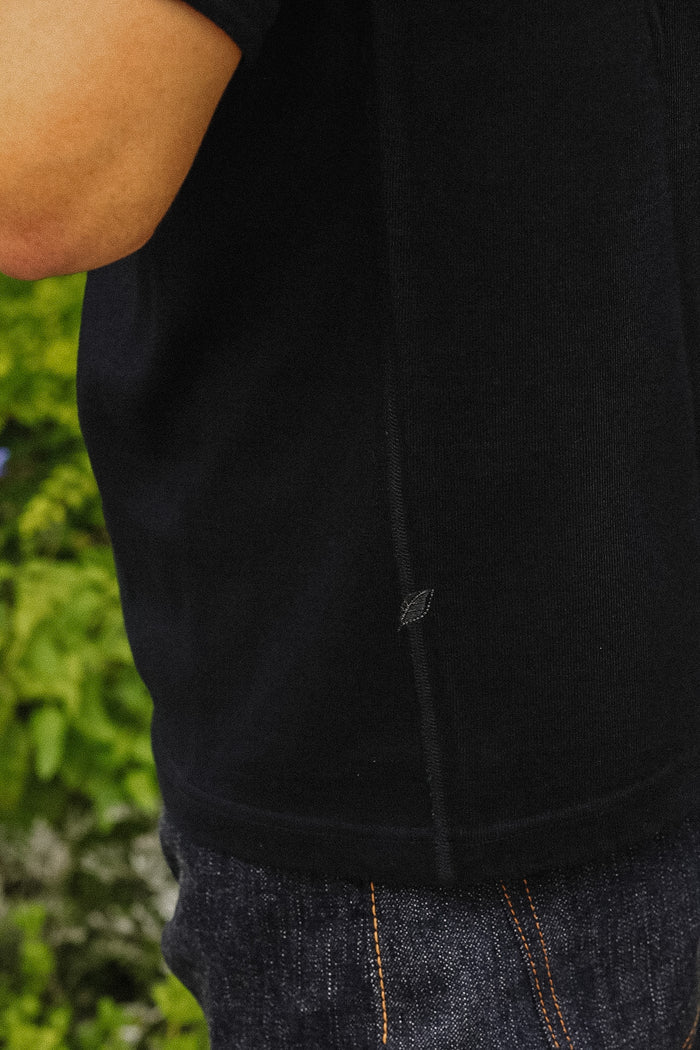 Close-up of a person wearing a black short-sleeve top and dark blue jeans, with a blurred green outdoor background.