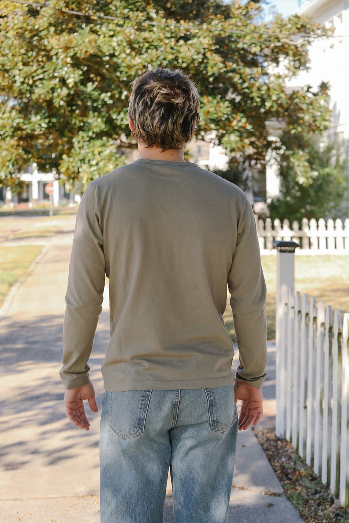 Man walking away from the camera on a sidewalk with trees and a white fence in the background