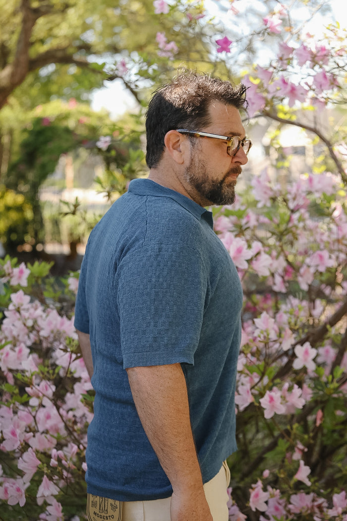 Man wearing glasses and a blue shirt standing among pink flowers