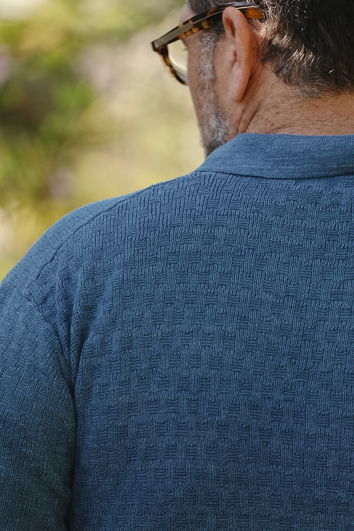 Man wearing a blue textured shirt with a blurred natural background