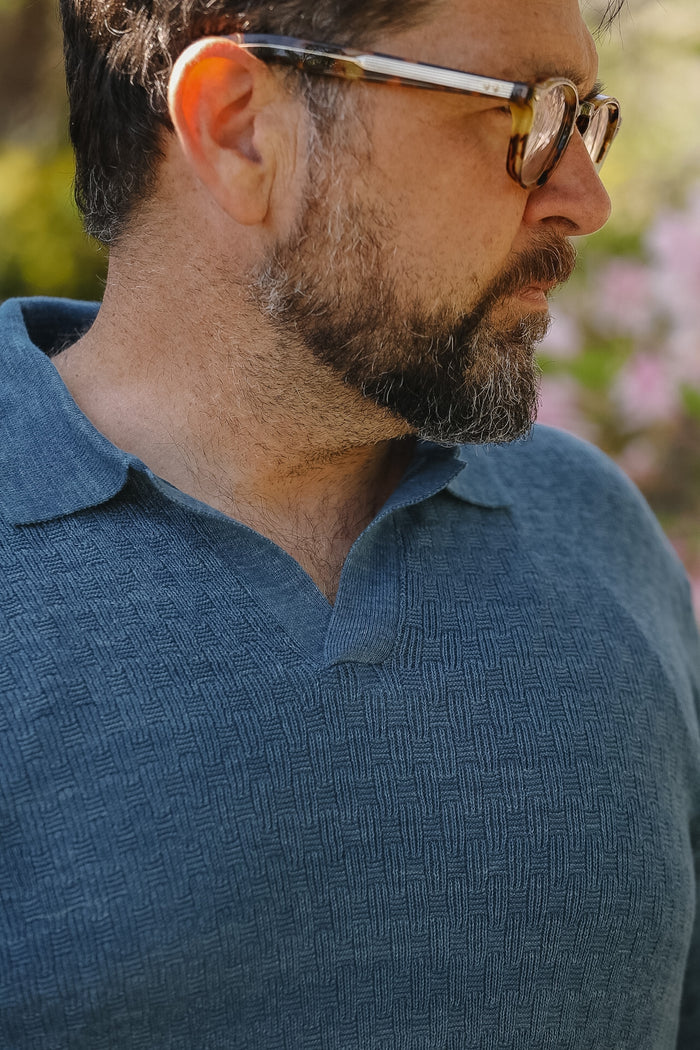 Man wearing sunglasses and a blue shirt with a blurred natural background