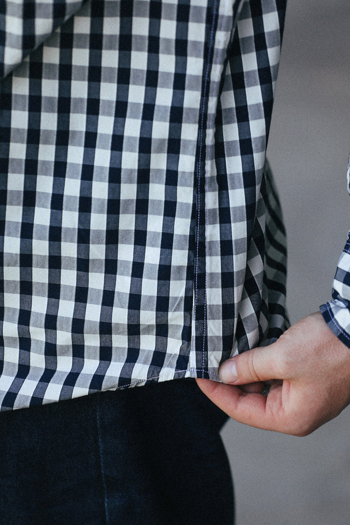 Close-up of a person wearing a black and white gingham plaid shirt, pulling the hem slightly to show the fabric and dark pants underneath.