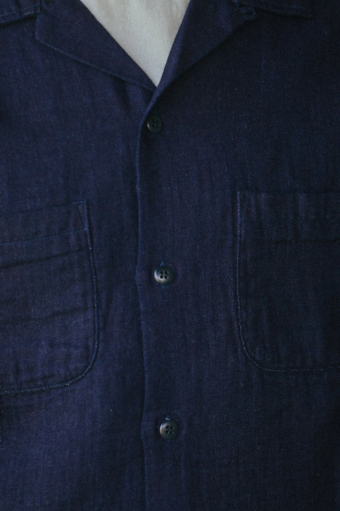 Close-up of a dark navy blue linen shirt with a button-down front, featuring two chest pockets and a pointed collar.