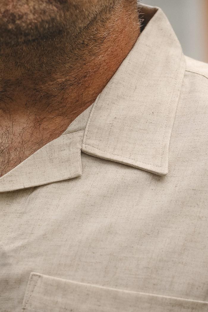 Close-up of a man wearing a light beige linen collared shirt, showing the collar, neck, and fabric texture.
