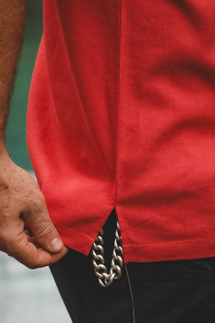 Close-up of a person wearing a bright red shirt with a silver chain detail hanging from the hem, paired with black pants.