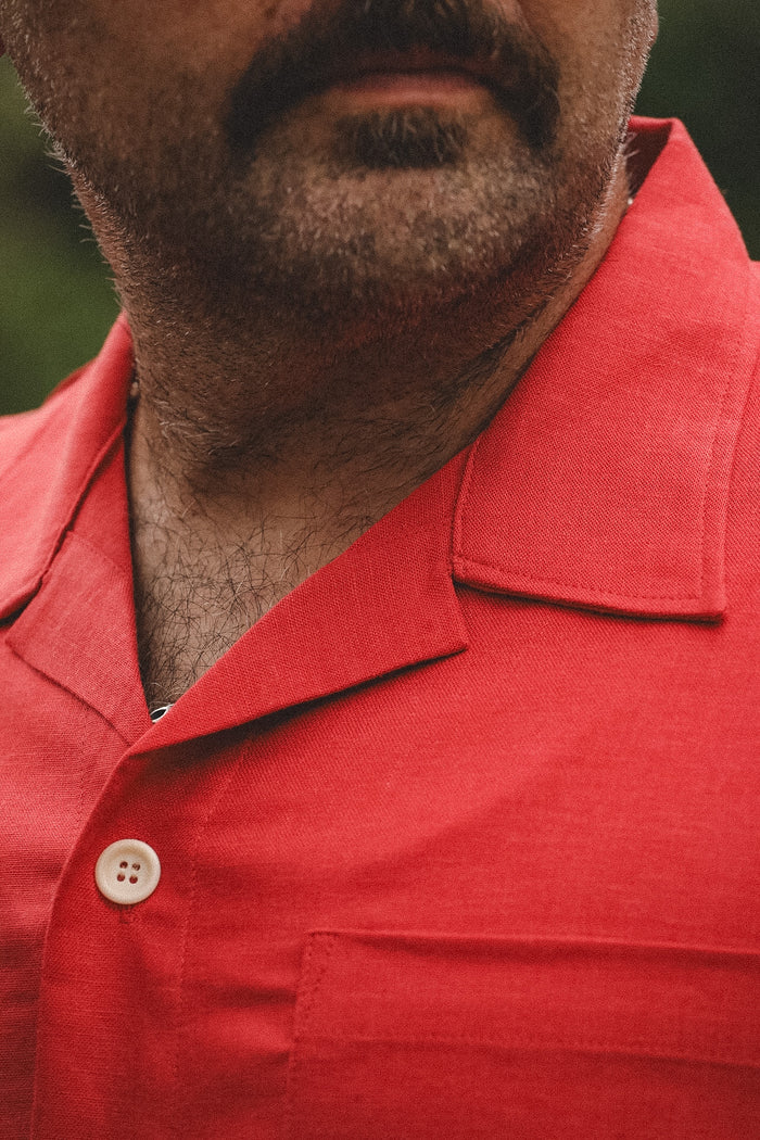 Close-up of a man wearing a red short-sleeve collared button-up shirt, showing the collar, chest pocket, and a white button.