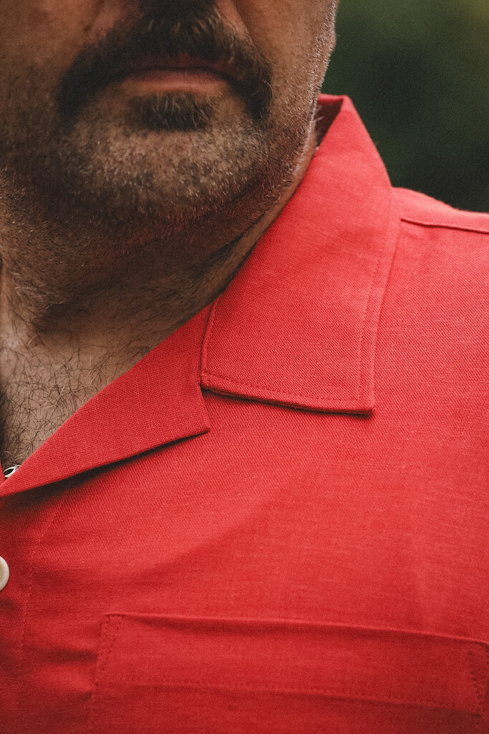 Close-up of a man wearing a bright red short-sleeve collared shirt, showing the collar, chest pocket, and part of his beard and mustache.