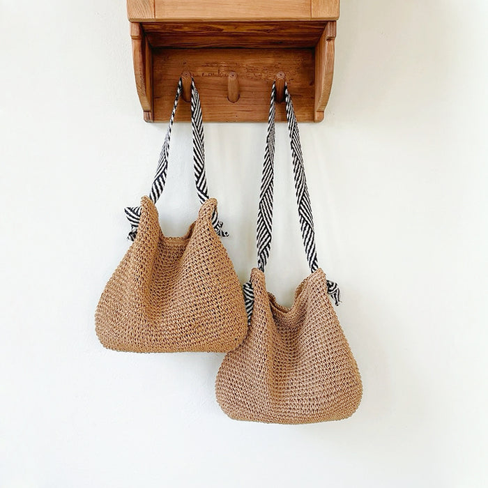 Two straw bags with different straps lengths hang on the wall: one features shoulder strap, the other has crossbody strap.