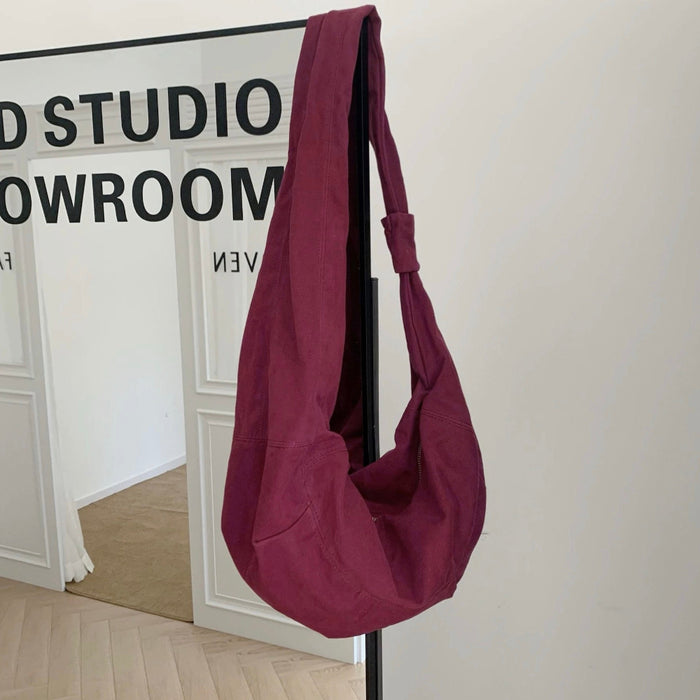Burgundy corduroy crescent bag hanging against a white gallery wall.