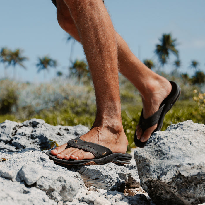 Close-up of a man's feet wearing black Fanning flip flops facing right, showcasing comfort and arch support for beach use.