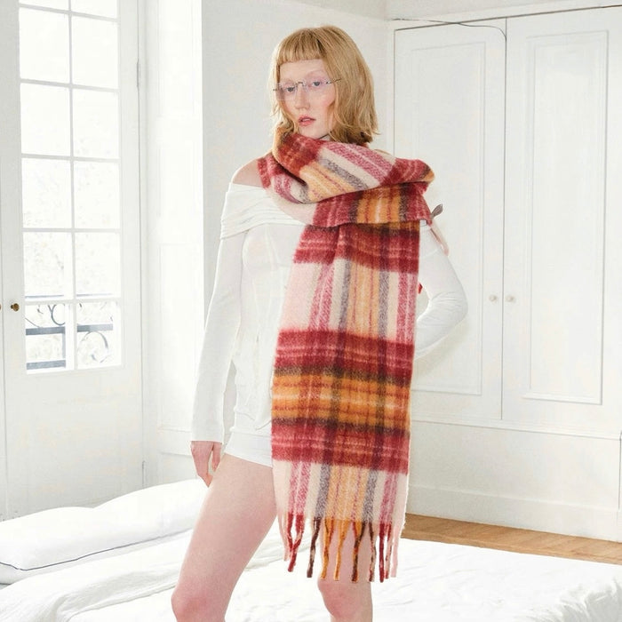 Model wearing long, wool blend Fiery Sunrise Plaid Scarf in red, orange, and pink tones with fringe in yellow.