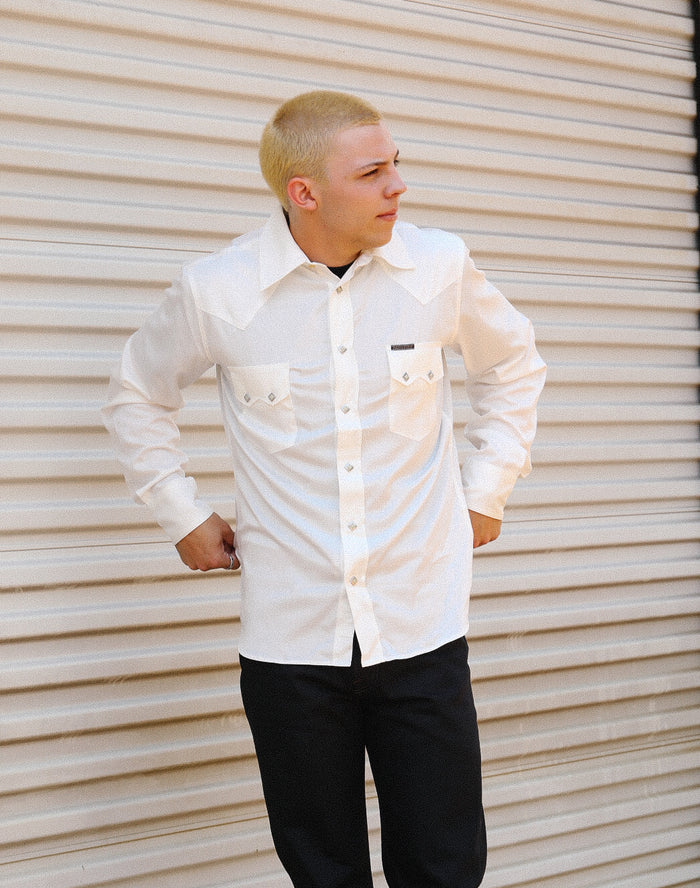 Man wearing a white Lindell Tencel cotton long-sleeve shirt with black pants against a beige corrugated metal background