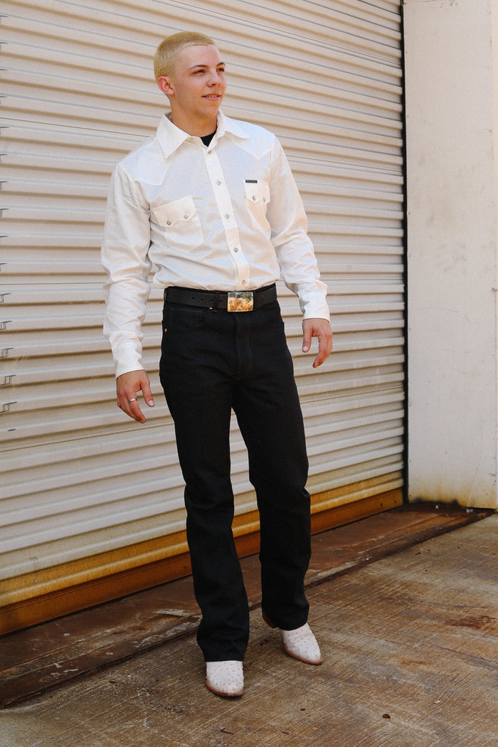 Man wearing white Tencel cotton shirt, black jeans, white boots, and decorative belt standing by metal roll-up door
