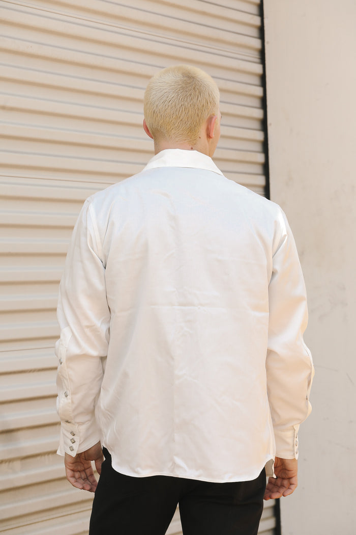 Back view of man wearing white Tencel cotton shirt with decorative cuffs, standing by beige metal shutter