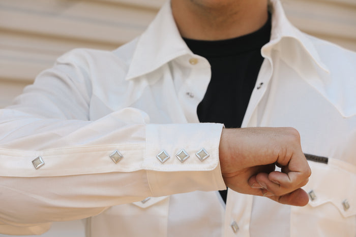 Close-up of a man wearing a white Lindell Tencel cotton shirt with diamond-shaped silver buttons, paired with a black undershirt