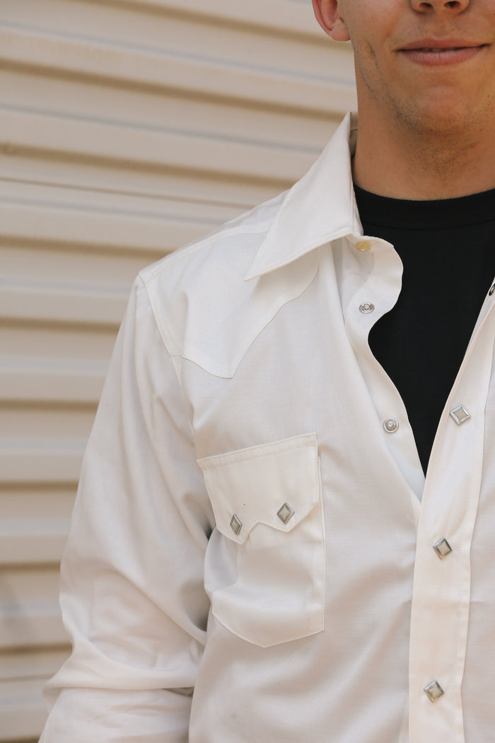 Close-up of a man wearing a white Lindell Tencel cotton shirt with diamond studs over a black T-shirt