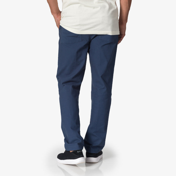 Rear view of a man wearing blue Matthew Twill Pant with black REEF sneakers facing away, showcasing comfort and casual style.