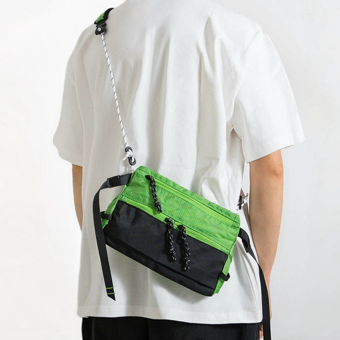 Model carrying a green and black nylon sling bag, utility crossbody style for urban travel.