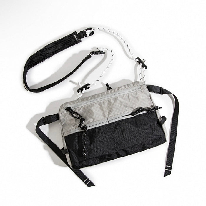 Angled view of grey utility sling bag showing three front zip pockets.