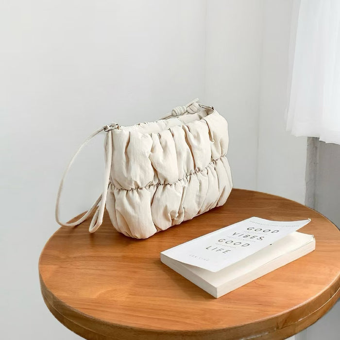 Close-up of beige pleated cloud bag with adjustable strap on a wooden table, ideal for errands.