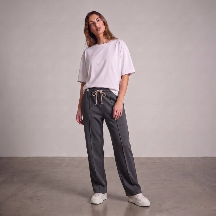 A woman modeling a light pink oversized t-shirt and dark gray drawstring baggy trouser, standing against a neutral studio backdrop l AH Urban Wear Pk