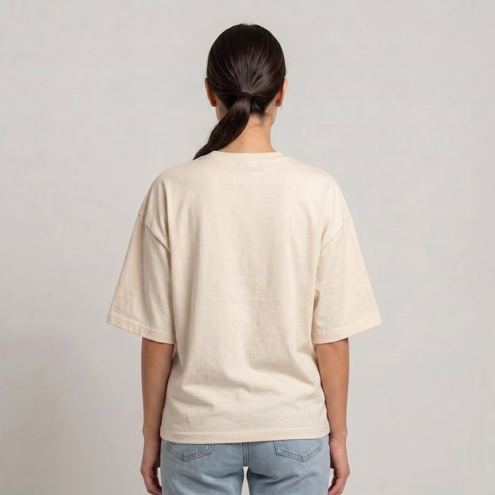 A person viewed from the back wearing an oversized cream-colored short-sleeve t-shirt and light blue jeans, set against a plain light gray studio background l AH Urban Wear